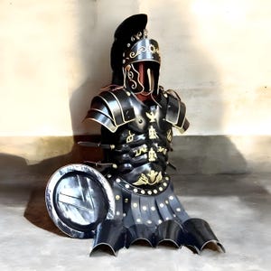 May include: A black and gold Roman armor set, including a helmet, breastplate, and skirt, with a matching shield. The armor features intricate gold detailing and is designed to resemble historical Roman military attire. The set is displayed on a mannequin.