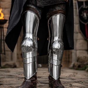 Handcrafted polished medieval steel leg greaves with adjustable leather straps, Gothic knight shin armor for LARP, cosplay, Renaissance fairs, reenactments, and historical costume.