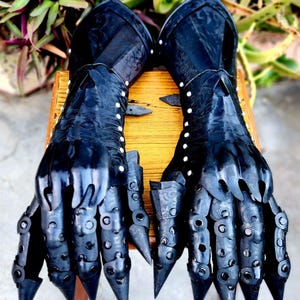 May include: A pair of black leather gauntlets with metal accents and spikes. The gauntlets are decorated with a floral pattern and have a textured surface.