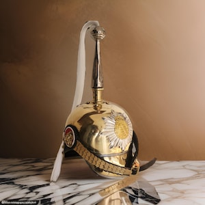 May include: A gold and silver helmet with a white plume. The helmet has a decorative band around the base and a large, silver star with a gold center.