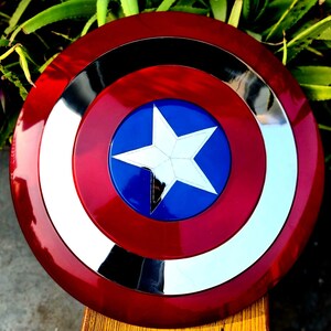 May include: A red, white and blue Captain America shield with a silver star in the centre. The shield is made of metal and has a shiny finish.