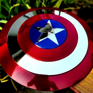 May include: A red, white and blue Captain America shield with a silver star in the centre. The shield is made of metal and has a shiny finish.