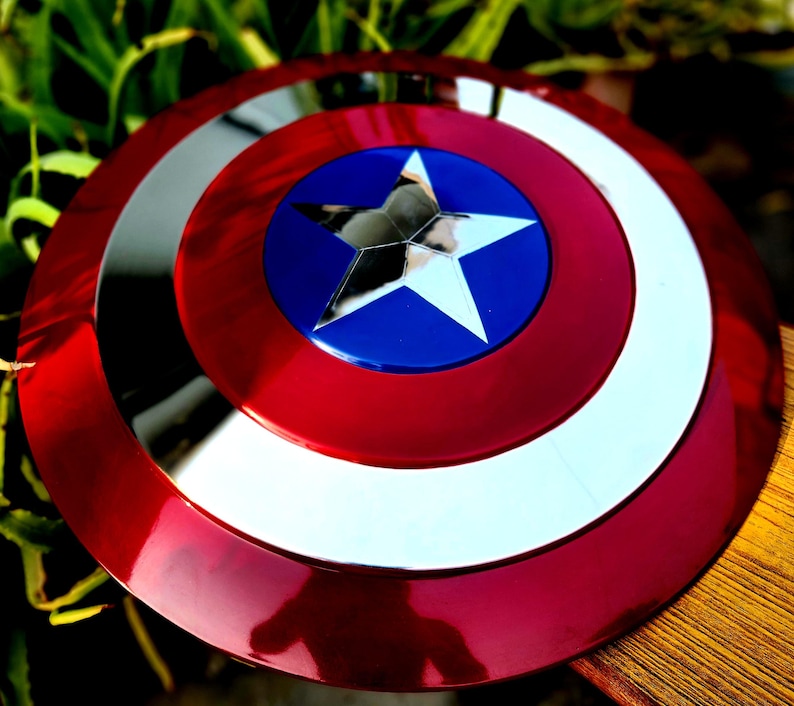 May include: A red, white and blue Captain America shield with a silver star in the centre. The shield is made of metal and has a shiny finish.