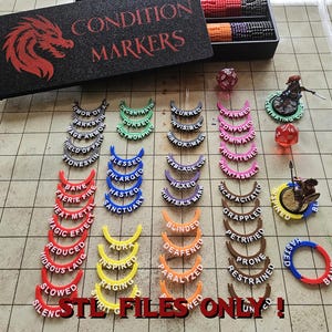 May include: A selection of colourful condition markers for tabletop gaming. The set includes curved markers with text such as "Blurred," "Charmed," and "Hasted," plus a storage box and dice. The markers are in various colours.