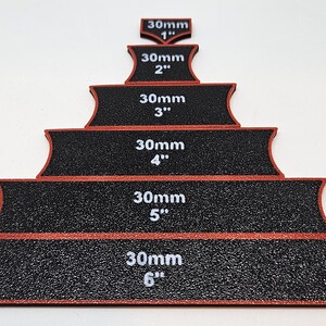 Op de afbeelding: Zes zwarte schuurblokken met rode randen, elk gelabeld met een maat in inches en millimeters. De blokken zijn in een piramidevorm gerangschikt, met het kleinste blok bovenaan en het grootste blok onderaan.