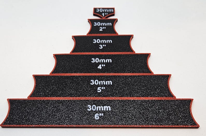 Op de afbeelding: Zes zwarte schuurblokken met rode randen, elk gelabeld met een maat in inches en millimeters. De blokken zijn in een piramidevorm gerangschikt, met het kleinste blok bovenaan en het grootste blok onderaan.