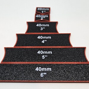 Op de afbeelding: Set van zes zwarte schuurbanden met rode randen, elk gelabeld met de maat in millimeters en inches. De banden zijn gerangschikt in een piramidevorm, met de kleinste band bovenaan en de grootste band onderaan.