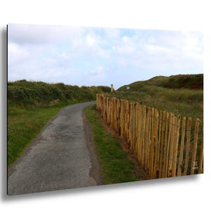 May include: A scenic landscape print featuring a winding asphalt path bordered by a wooden fence and lush green vegetation. The sky is overcast with a mix of clouds. A road sign is visible in the distance.