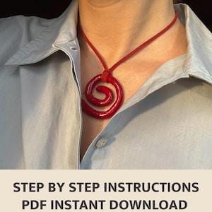 Op de afbeelding: Een opvallende rode spiraalvormige hangerketting. De hanger hangt aan een bijpassend rood koord, wat een gedurfd contrast vormt met het lichtblauwe overhemd. De ketting heeft een glanzende afwerking en een uniek ontwerp. De tekst: STEP BY STEP INSTRUCTIONS PDF INSTANT DOWNLOAD.