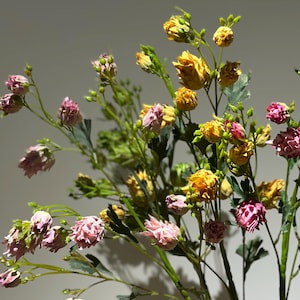 Op de afbeelding: Een boeket kunstbloemen in een vaas. De bloemen zijn roze en geel en hebben een delicate, gekrulde uitstraling.