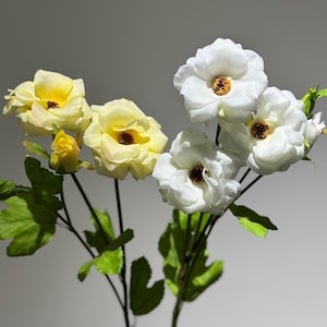 May include: A bouquet of artificial flowers with white and yellow blooms. The flowers have a realistic appearance and are arranged in a vase.