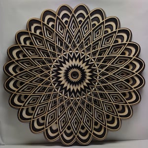 May include: A black and white geometric mandala wall art piece made of wood. The design features a repeating pattern of overlapping circles and diamonds.