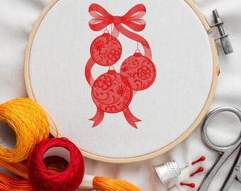 Peut inclure: Broderie d'ornements de Noël rouges sur tissu blanc tendu dans un cercle à broder en bois. Le motif présente trois ornements détaillés suspendus à un nœud et un ruban rouges. Des fournitures de broderie, dont du fil et des ciseaux, sont visibles.