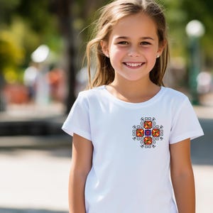 May include: White t-shirt with a colorful embroidered design on the front. The design features a geometric pattern with red, orange, yellow, blue, and green colors.