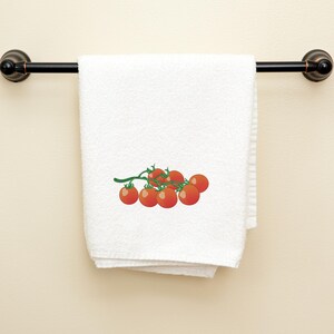 May include: White bath towel with a decorative embroidered sprig of red cherry tomatoes and green stems. The towel is hanging on a black metal towel bar. The towel is folded and hanging on a wall.