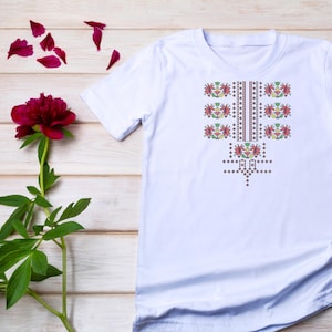 May include: White t-shirt with a colourful embroidered design featuring flowers and geometric patterns.