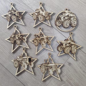 Pode incluir: Uma coleção de enfeites de madeira em forma de estrela com tratores. Cada enfeite apresenta um design detalhado de trator, com um pequeno orifício para pendurar. Os enfeites são feitos de madeira clara.