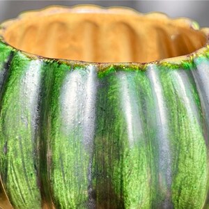 May include: A ceramic bowl with a ribbed exterior, featuring a gradient of green hues. The interior is a warm, golden color. The bowl's design is reminiscent of a pumpkin, making it suitable for decorative purposes.
