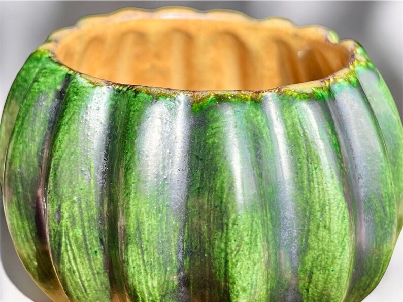 May include: A ceramic bowl with a ribbed exterior, featuring a gradient of green hues. The interior is a warm, golden color. The bowl's design is reminiscent of a pumpkin, making it suitable for decorative purposes.