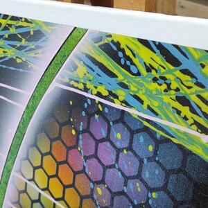 Op de afbeelding: Abstract schilderij op canvas met een zwarte achtergrond, groene, blauwe en gele verfspatten en een regenboogkleurig honingraatpatroon.