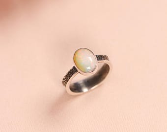 Può includere: Un anello d'argento con una fascia testurizzata e una pietra di opale di forma ovale.
