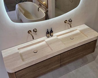 May include: A double vanity featuring a light beige stone countertop with two integrated rectangular sinks, mounted above a dark wood cabinet. Above the vanity is an organic-shaped, wall-mounted mirror with integrated LED backlighting.