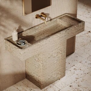 Puede incluir: Un lavabo rectangular de piedra con una balda integrada y un grifo monomando. El lavabo es de color beige claro y tiene una base de pedestal a juego. Un dispensador de jabón y un plato pequeño con jabón están en la balda.