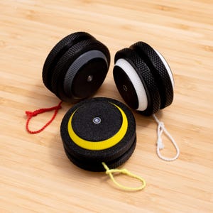 Może przedstawiać: Trzy jojo z różnokolorowymi sznurkami i wzorami. Jojo są czarne z białym lub żółtym akcentem.