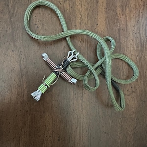 May include: A green rope necklace with a cross pendant made of wire and nails. The cross is wrapped in green and copper wire.