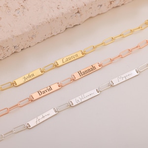 May include: Three gold chain bracelets with personalized nameplates. The top bracelet is gold, the middle bracelet is rose gold, and the bottom bracelet is silver. The nameplates are engraved with the names "John", "Lauren", "David", "Hannah", "William", "Megan", and "Andrew".