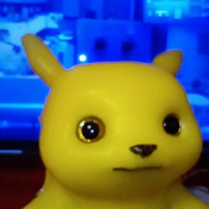 Puede incluir: Un juguete de goma amarillo con una cara de dibujos animados, ojos grandes negros con bordes dorados y una nariz negra. El juguete tiene una sonrisa simple.