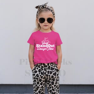 Puede incluir: Una persona joven con una camiseta magenta con el texto "Your StandOut Design Here" en blanco. También lleva pantalones con estampado de leopardo, gafas de sol y una diadema con estampado de leopardo.