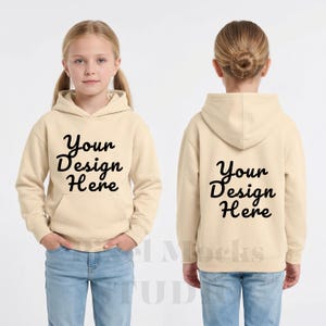 以下が含まれることがあります： 前面と背面に黒い筆記体で「Your Design Here」という文字が入ったベージュ色のフード付きスウェットシャツ。明るい青色のジーンズを履いた若い人が着ています。背景は無地の白です。