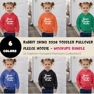 Pode incluir: Imagem de maquete de seis hoodies de lã para crianças pequenas em várias cores: vermelho, laranja, verde, azul, carvão e rosa. Cada hoodie apresenta o texto "Your Design Here" em branco. A imagem também inclui o texto "Rabbit Skins 3326 Toddler Pullover Fleece Hoodie - Mockups Bundle".
