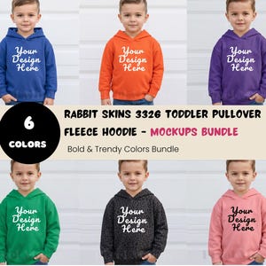 Pode incluir: Seis hoodies de lã polar para crianças pequenas em várias cores: azul, laranja, roxo, verde, preto e rosa. Cada hoodie apresenta o texto "Your Design Here". A imagem também inclui o texto "RABBIT SKINS 3326 TODDLER PULLOVER FLEECE HOODIE - MOCKUPS BUNDLE".