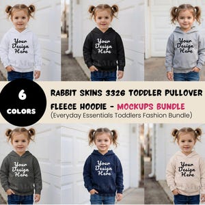 May include: A mockup image of six toddler fleece hoodies in various colors: white, black, gray, charcoal, navy, and beige. Each hoodie features the text "Your Design Here". The image also includes text that reads "Rabbit Skins 3326 Toddler Pullover Fleece Hoodie - Mockups Bundle".