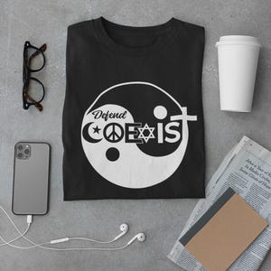 Könnte beinhalten: Schwarzes T-Shirt mit einem weißen Yin-Yang-Symbol und dem Text "Defend Coexist" im Symbol. Das Symbol enthält einen Halbmond, ein Peace-Zeichen, einen Davidstern und ein Kreuz.