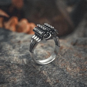 Puede incluir: Un anillo de plata con un diseño de motor detallado. El motor está hecho de plata y tiene un acabado negro. El anillo es una pieza llamativa para los entusiastas de los coches.