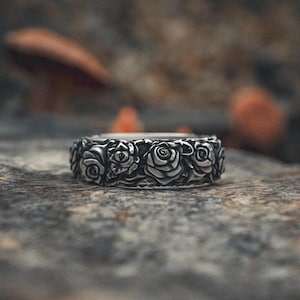 Puede incluir: Un anillo de plata con un diseño detallado de rosas alrededor de la banda.