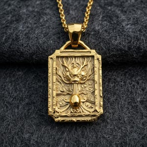 Puede incluir: Collar con colgante dorado con un colgante rectangular con un diseño de dragón en relieve. El dragón está centrado en el colgante, con detalles intrincados. El collar tiene una cadena dorada a juego.