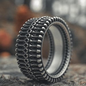 Könnte beinhalten: Ein silberner Ring mit einem strukturierten, skelettartigen Design. Der Ring besteht aus mehreren Bändern, die einen geschichteten Effekt erzeugen.