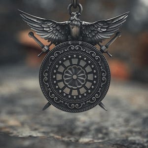 May include: A silver pendant necklace featuring a detailed eagle with outstretched wings atop a shield design. Two swords are crossed behind the shield. The pendant hangs from a chain.