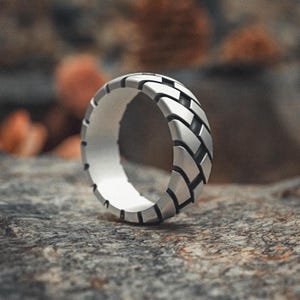 May include: A silver ring with a textured design that resembles a tyre tread.