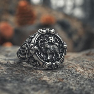 May include: A silver ring with an ornate design featuring a lamb with a cross and the text "ECCE AGNUS DEI - QUI TOLLIT PECCATA MUNDI".
