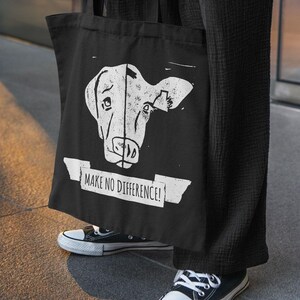 Könnte beinhalten: Schwarze Tragetasche mit einem weißen, verblassten Kuhgesicht-Grafik. Der Text "MAKE NO DIFFERENCE!" ist darunter gedruckt. Die Person trägt eine schwarze Hose und schwarz-weiße Turnschuhe.
