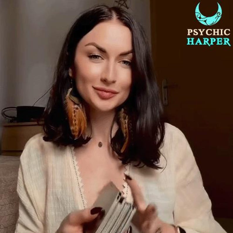 Op de afbeelding: Een vrouw met lang donker haar, die een wit shirt en veren oorbellen draagt, houdt een deck tarotkaarten vast. De tekst "PSYCHIC HARPER" is zichtbaar in de rechterbovenhoek van de afbeelding.