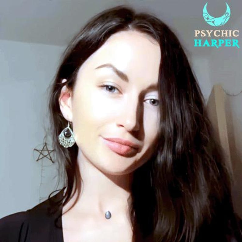 Op de afbeelding: Een vrouw met lang donker haar glimlacht naar de camera. Ze draagt een zwart shirt en heeft een klein zilveren ketting met een hanger. De tekst "PSYCHIC HARPER" is zichtbaar in de rechterbovenhoek van de afbeelding.