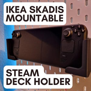 Może przedstawiać: Czarna konsola do gier Steam Deck zamontowana na białej ścianie z płyty perforowanej za pomocą czarnego, montowanego na ścianie uchwytu IKEA SKADIS. Na zdjęciu widoczny jest tekst "IKEA SKADIS MOUNTABLE" i "STEAM DECK HOLDER".