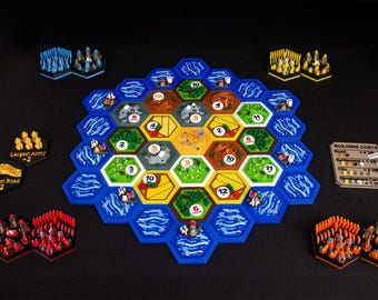 May include: A board game set featuring a hexagonal modular board with terrain tiles, numbered tokens, and miniature game pieces in blue, yellow, red, and orange. Includes a building costs reference card and two special victory point tiles.