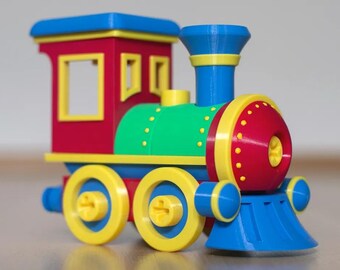 May include: A toy train engine featuring a red cabin with yellow window frames, a green cylindrical boiler, and a red front nose with yellow dots. The locomotive has blue wheels with yellow rims, a blue smokestack, and a blue cowcatcher at the front.